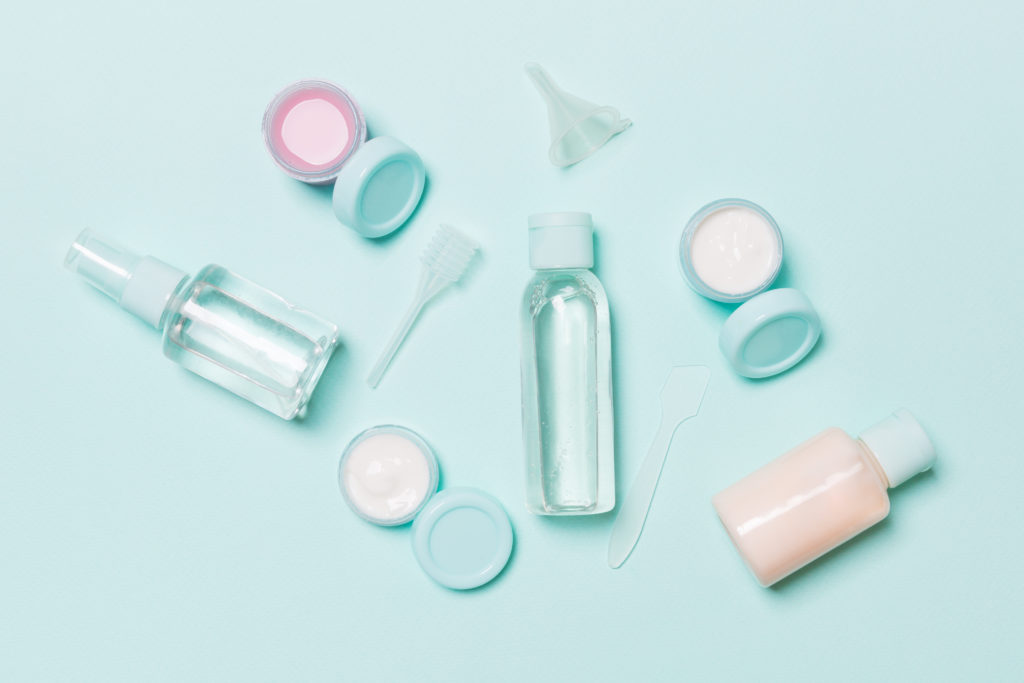Various travel toiletry bottles laid on out a teal backdrop