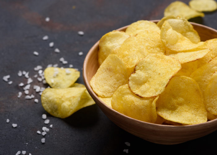 High angle view of bowl of potato chips with salt surrounding on table