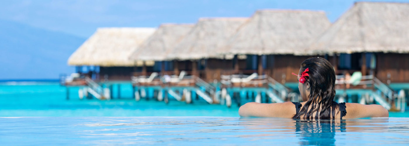 Woman in swimming pool overlooking a line of overwater bungalows