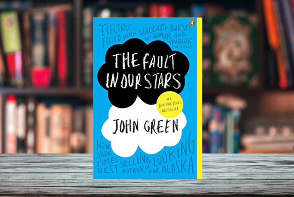 Cover of John Green's book The Fault in Our Stars superimposed on a bookshelf with shelves of books in the background