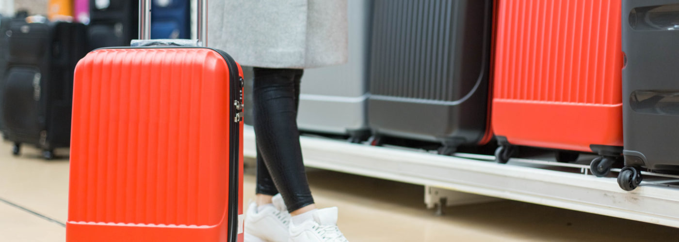 Close up of woman testing out rolling luggage in front of a rack of rolling luggage for sale