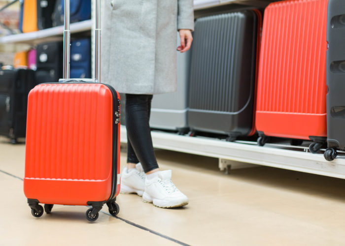 Close up of woman testing out rolling luggage in front of a rack of rolling luggage for sale