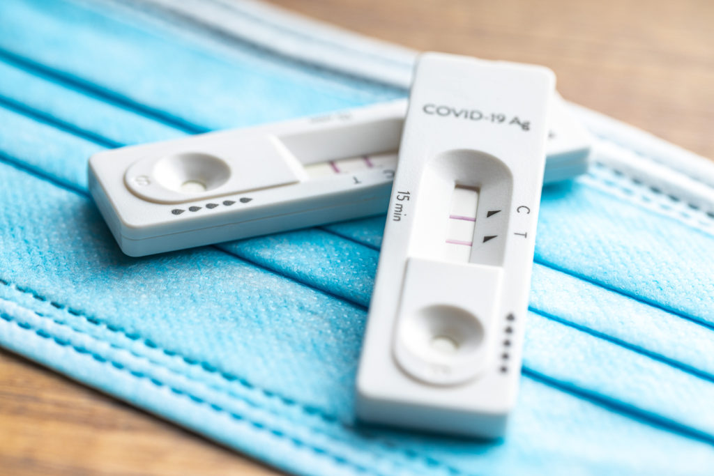 Two positive COVID tests on top of a blue medical face mask