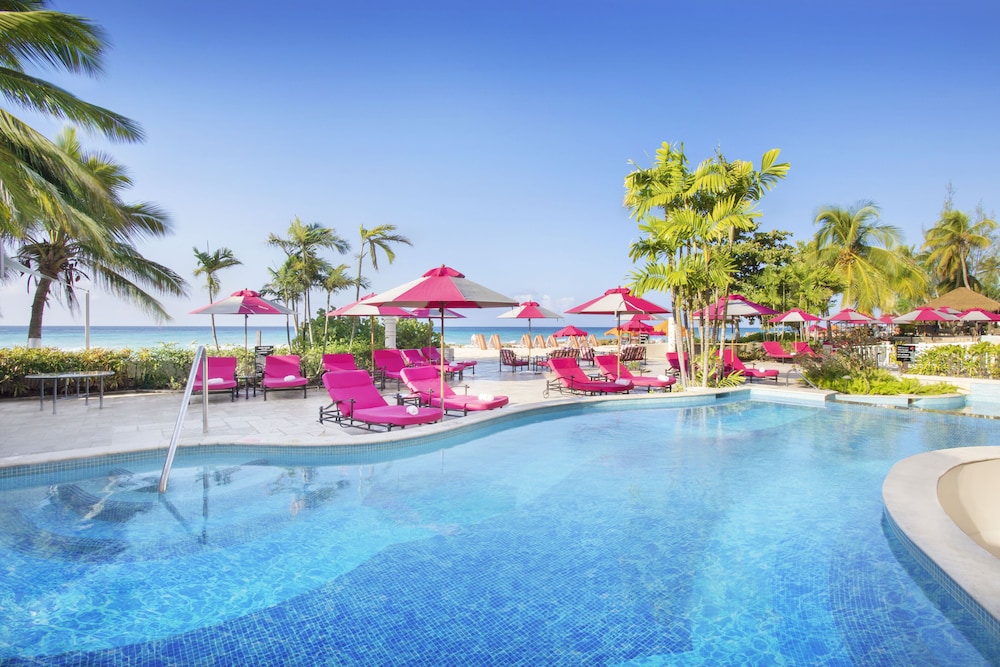 Pool surrounded by palm trees and pink lounge chairs at O2 Beach Club & Spa by Ocean Hotels All-Inclusive, Bridgetown, Barbados