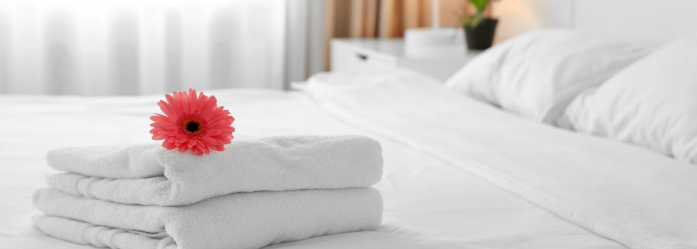 Red flower on a stack of white towels on a hotel bed with white bedspread