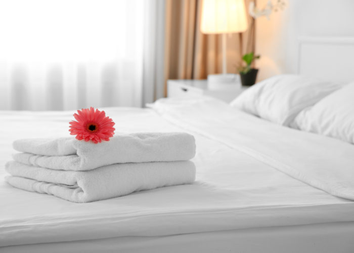 Red flower on a stack of white towels on a hotel bed with white bedspread