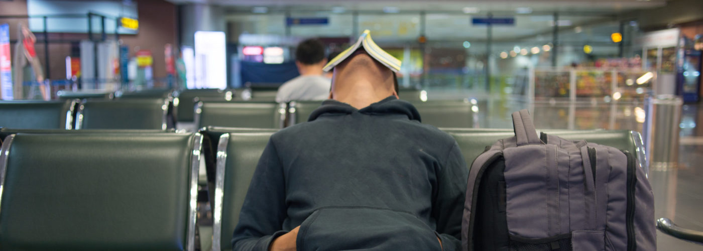 Person sleeping in airpot with a book propped on their face