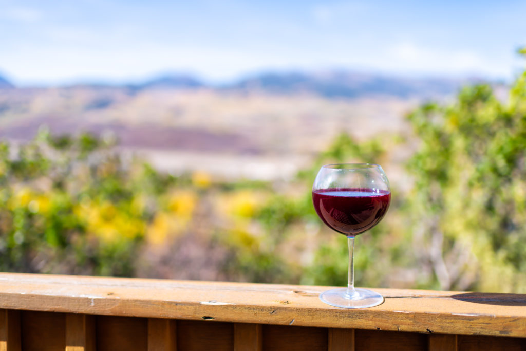 Red wine glass on a porch railing with trees out of focus in the background