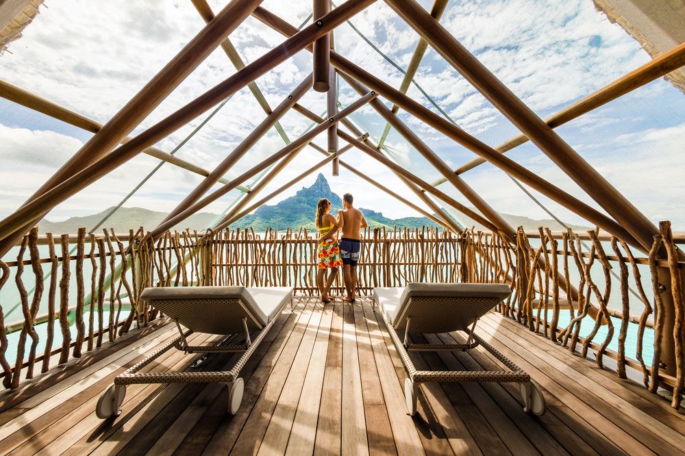 Couple on wooden deck overlooking the water at InterContinental Bora Bora Resort & Thalasso Spa, Motu Piti Aau, French Polynesia