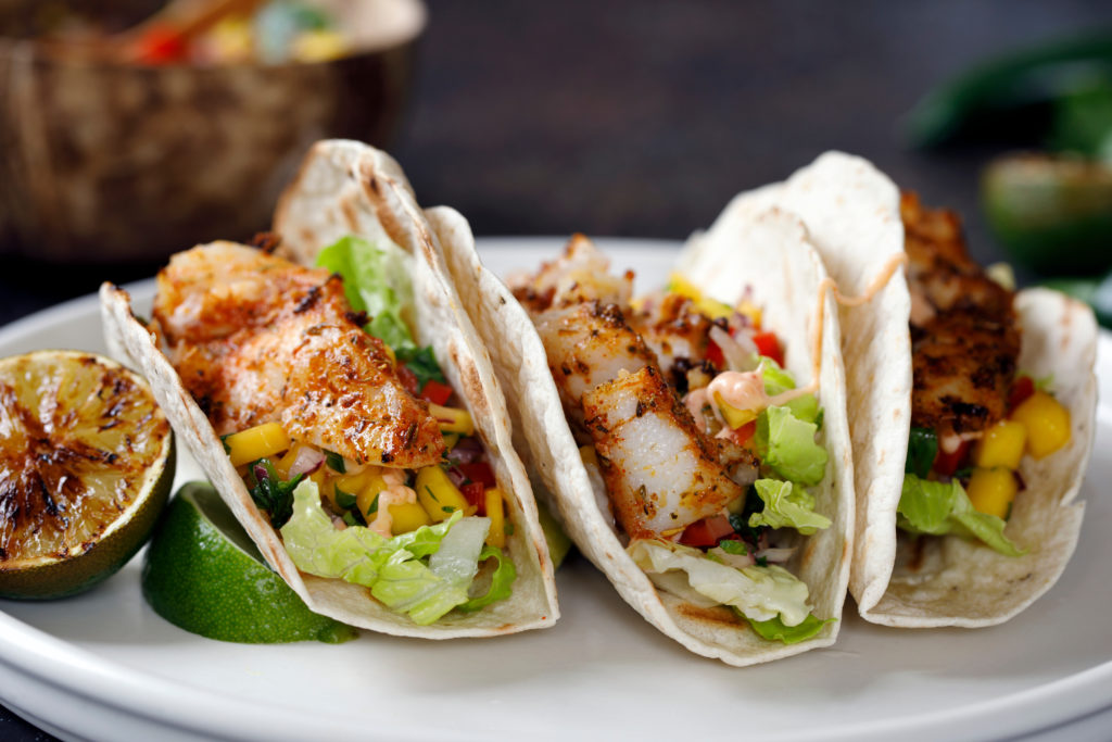 Three fish tacos with mango salsa on a white plate