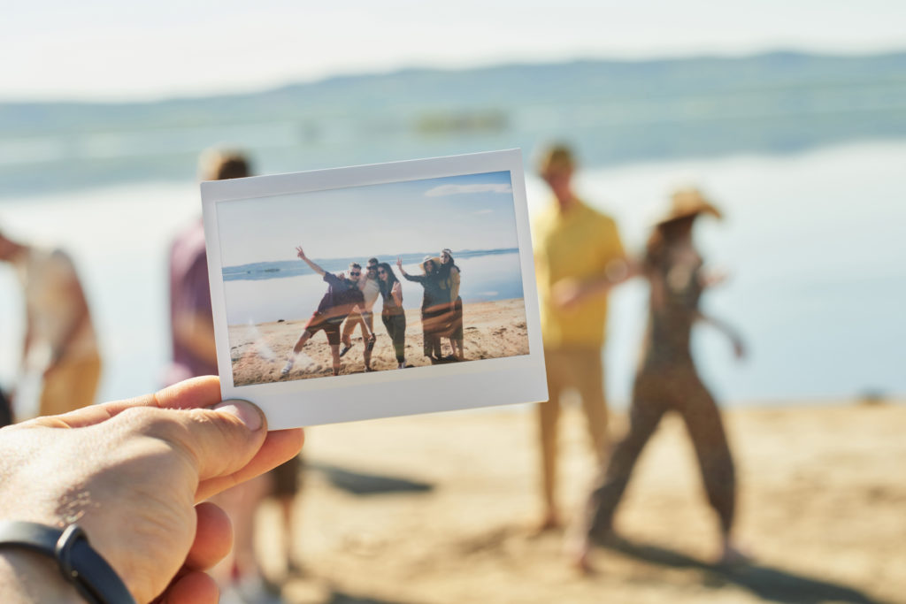 Person holding a polaroid photo of friends posing in a group up to the camera while the friends in the photo disperse in the background