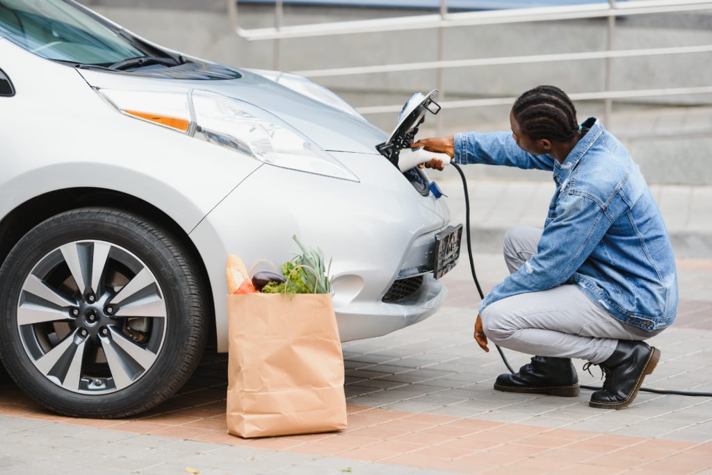 Man charging his electric car next to bag of groceries on the ground