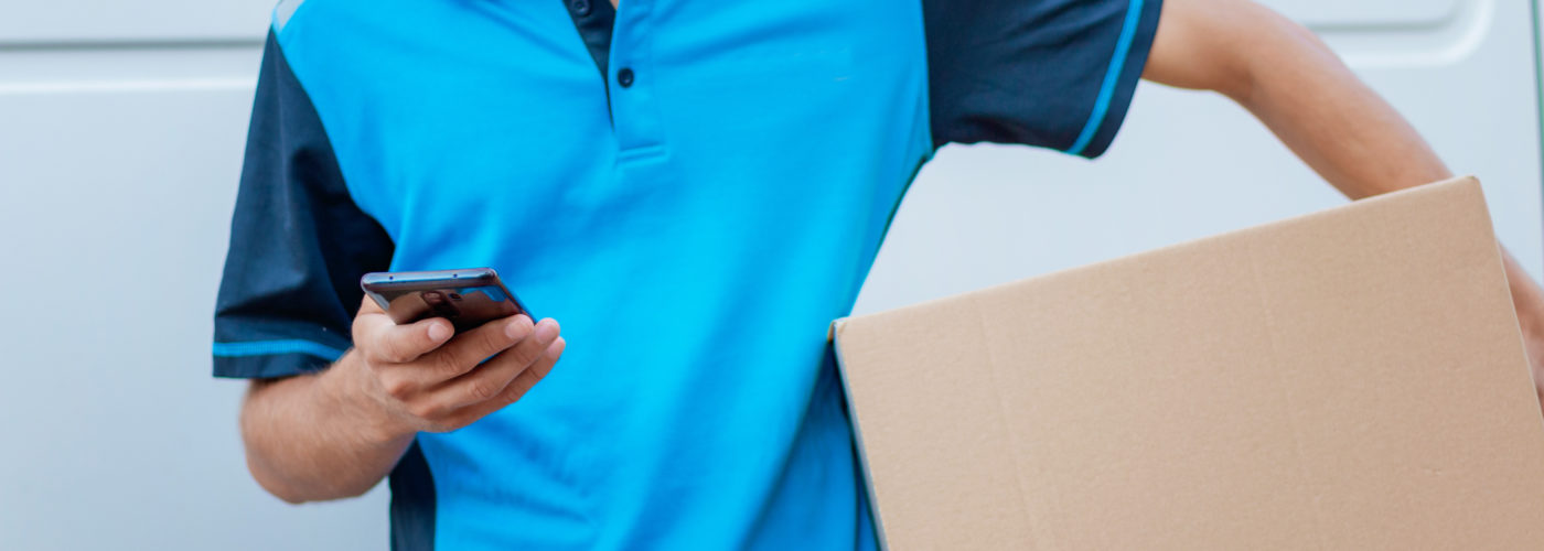 Close up of a man in a blue shirt reading on his phone while delivering a package