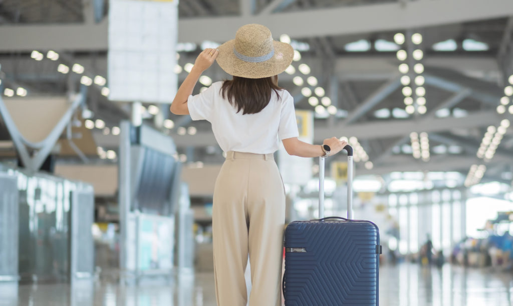 Woman wearing a sunhat and standing with her luggage in the middle of an airport terminal