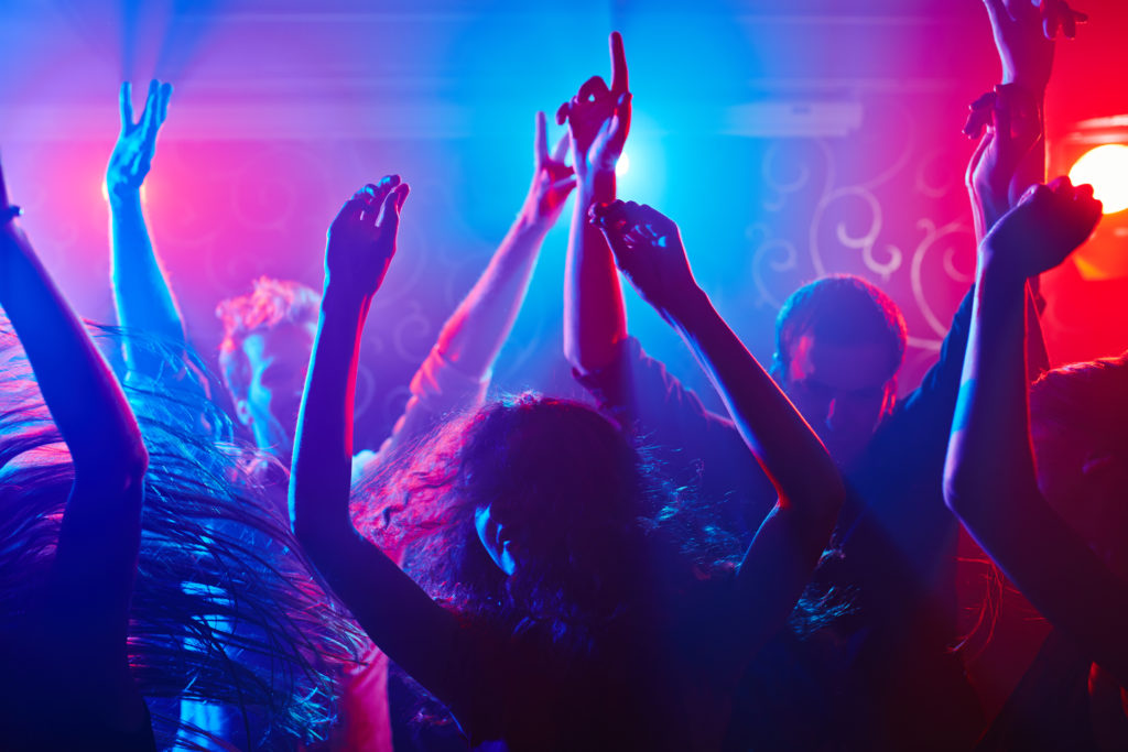 Silhouettes of dancers in a nightclub under pink and blue lights