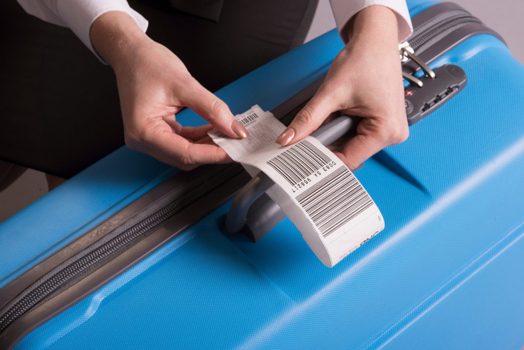 Close up of person attaching a luggage tag to a blue hardsided suitcase