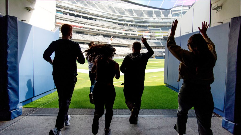 Four people running out onto the field o SoFi Stadium in Inglewood, Los Angeles, California