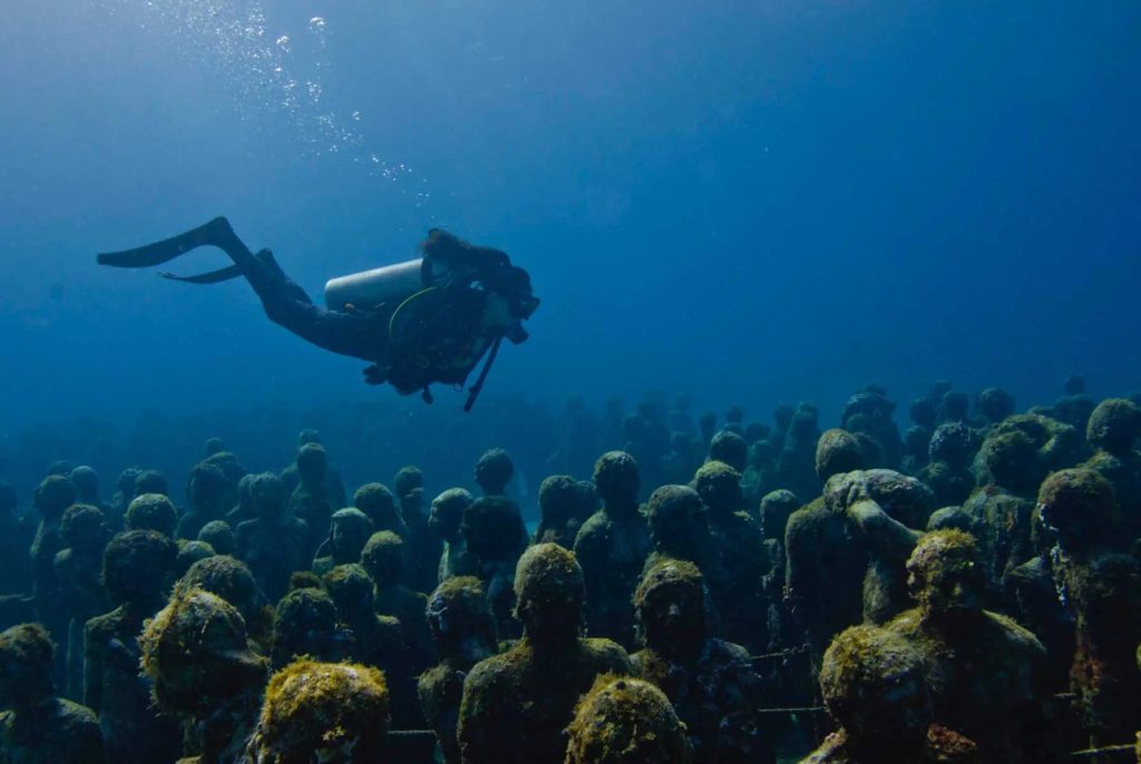 Underwater diver swimming over art installment La Evolución Silenciosa by artist Jason Decaires Taylor at the Aquaworld art exhibition in Cancún, Mexico