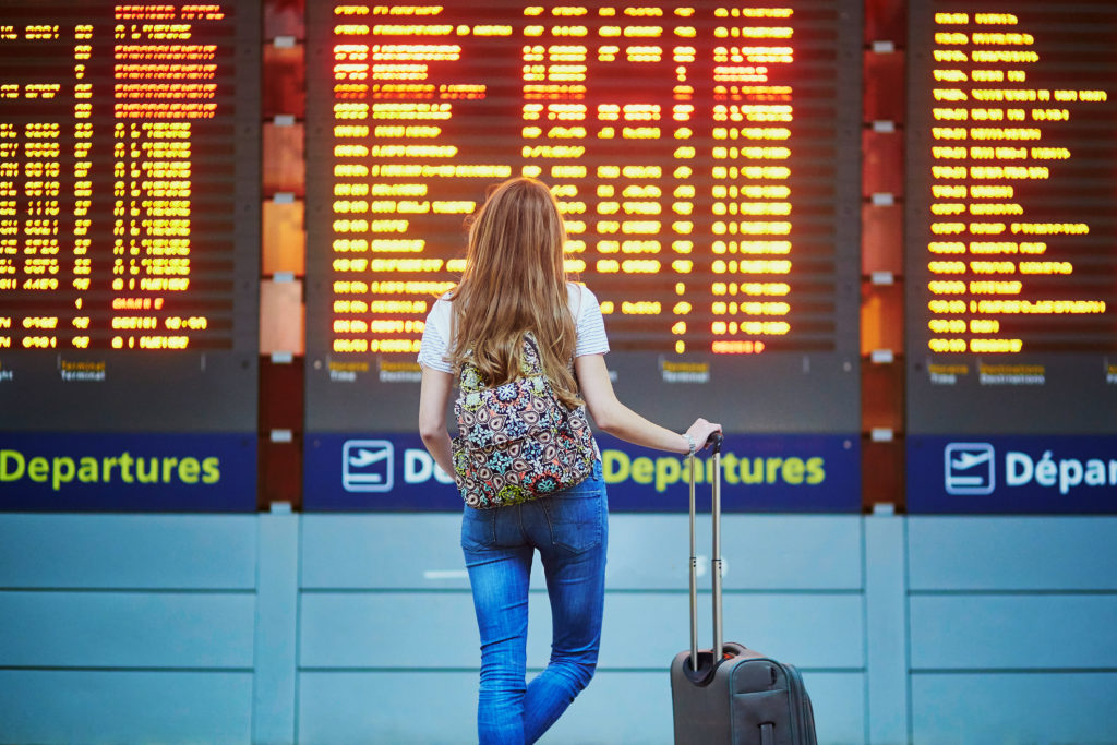 Woman holding rolling luggage looking at a departures board in an international airport