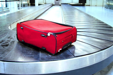 Single red suitcase on an otherwise empty baggage carousel