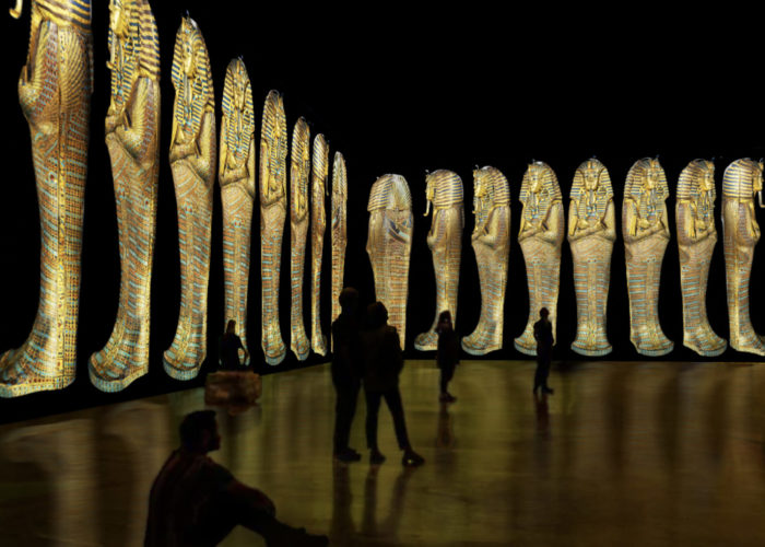 Images from inside the Beyond King Tut: The Immersive Experience, showing silhouettes of people looking at projections of sarcophagi lining the walls