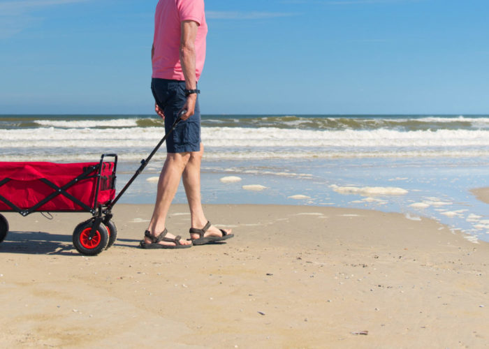 Senior citizen walking along the coast with a beach cart