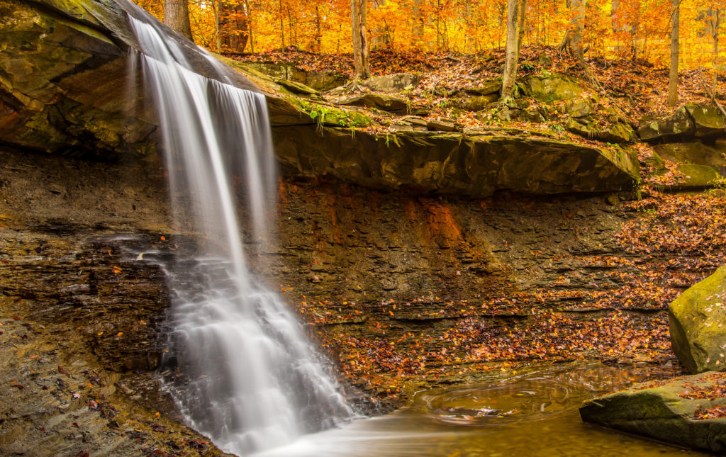 Waterfall surrounded by orange fall foliage and fallen leaves in Cuyahoga Valley National Park, Ohio