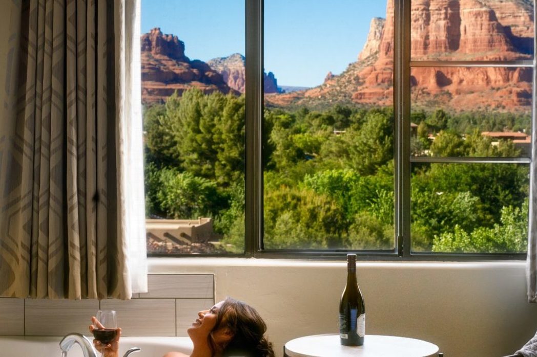 Woman relaxing in bathtub next to a window with views of large rock formation at the Hilton Sedona Resort at Bell Rock, Arizona