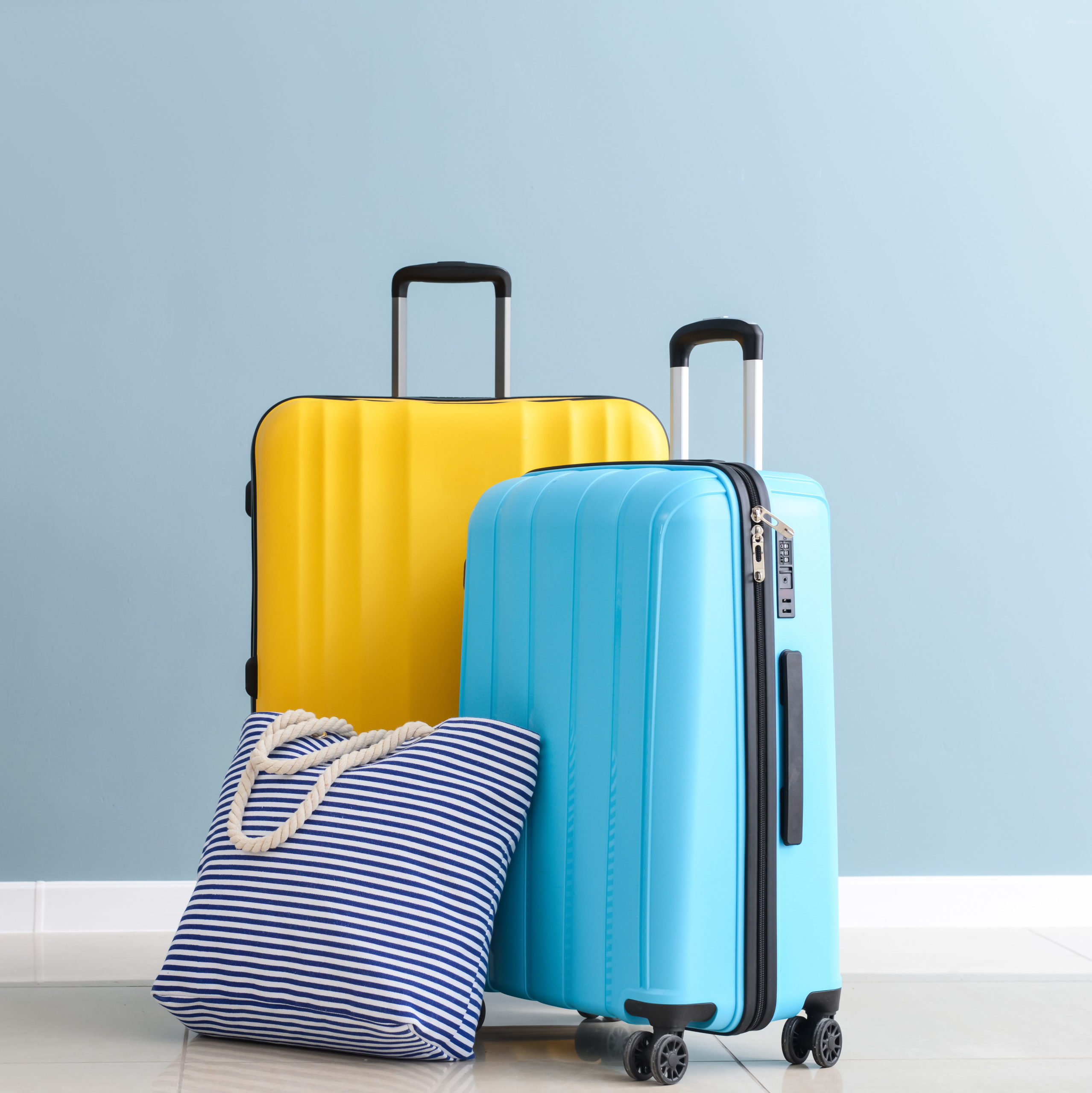 A yellow suitcase, a blue suitcase, and a striped tote bag sitting in a blue room