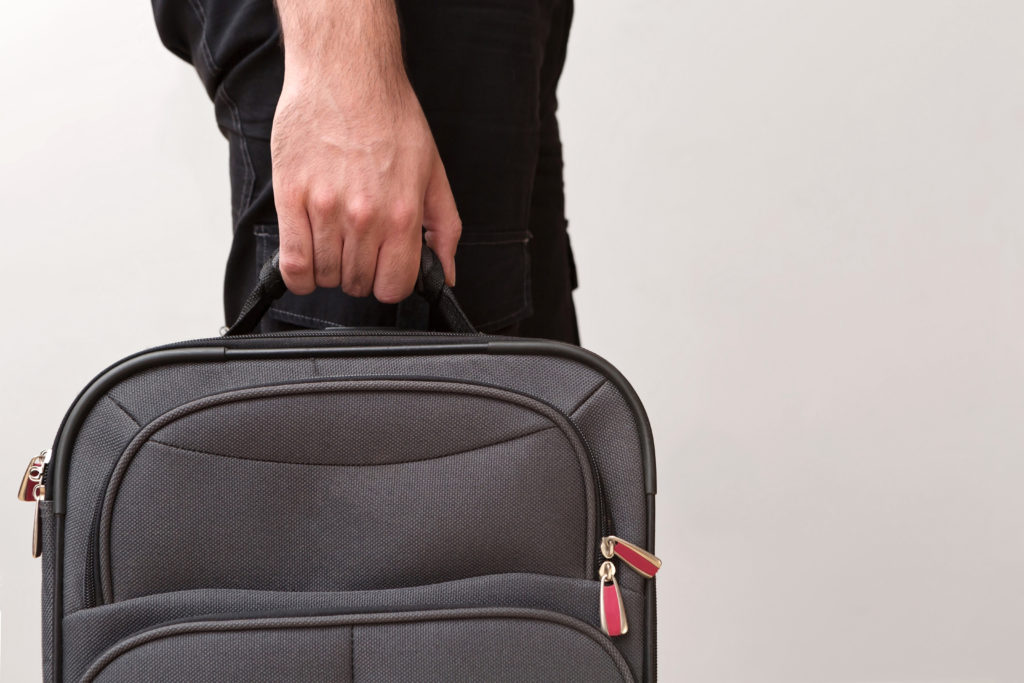 Close up of hand holding a grey suitcase against a grey wall