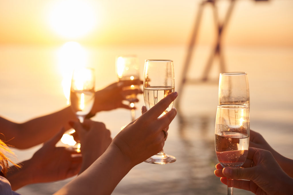 Close up of hands clinking glasses of champagne together at sunset on a beach