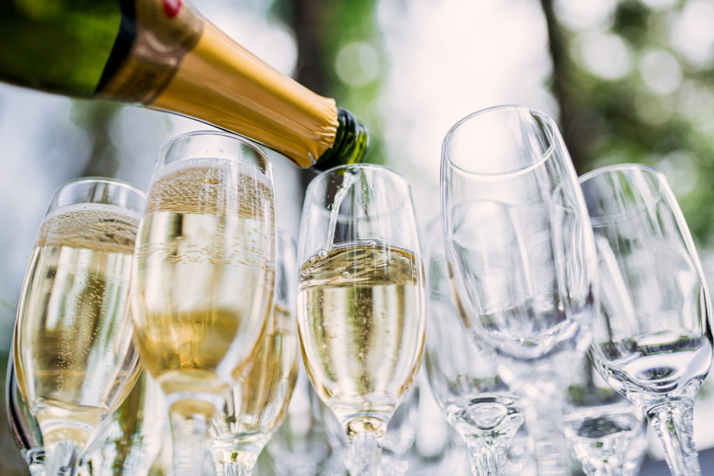 Close up of bottle of champagne being poured into several champagne glasses