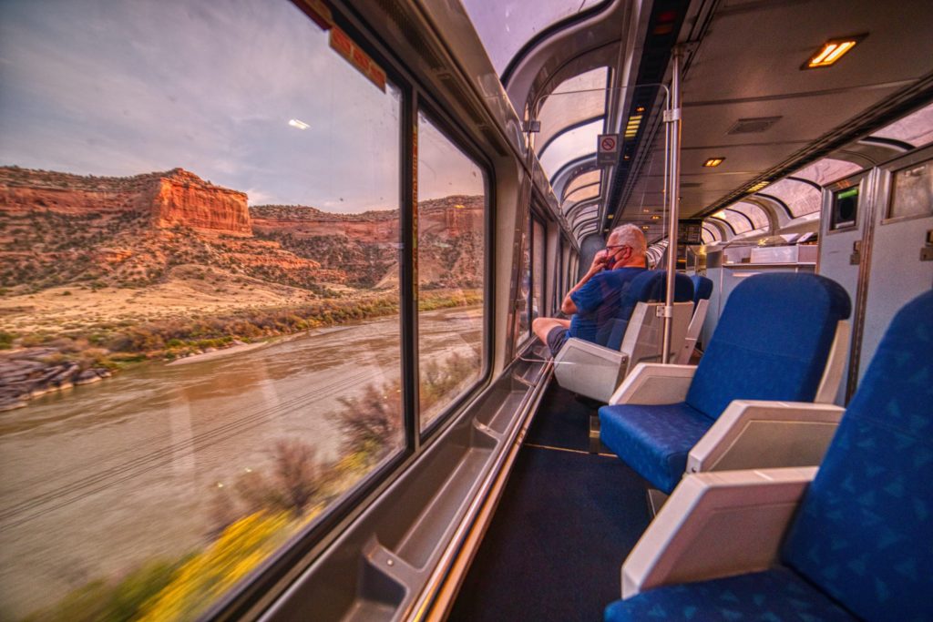 Man sitting in empty Amtrak train car looking out on a desert landscape