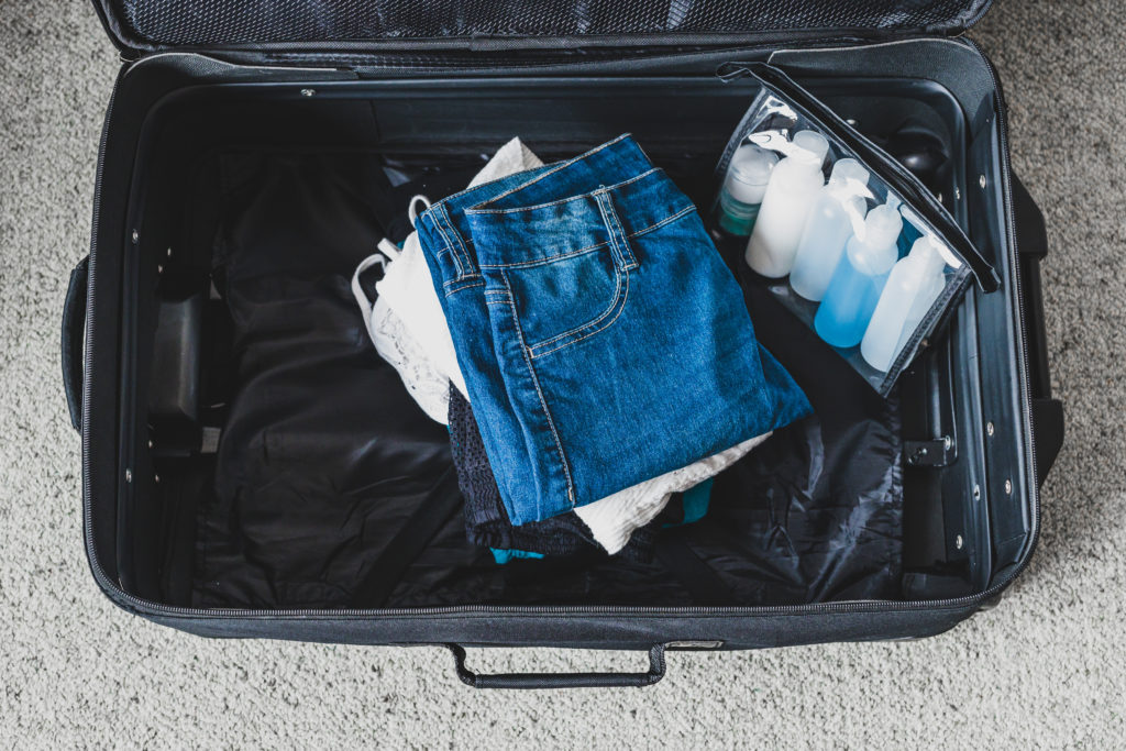 Aerial view of mostly empty suitcase, with a few clothes and TSA-approved liquid bottles in a clear bag.