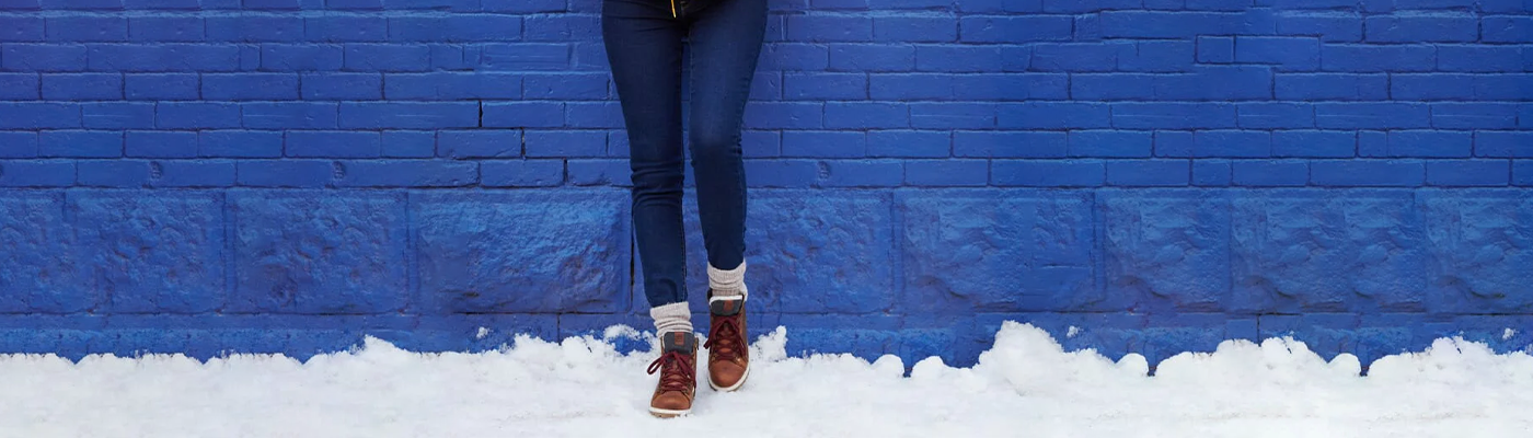 Close up of person leaning against a blue brick wall in the snow wearing Kamik Rouge Hike 3 boots