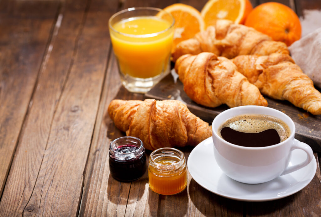 Espresso, jams, oranges and orange juice, and pastries laid out on a wooden table