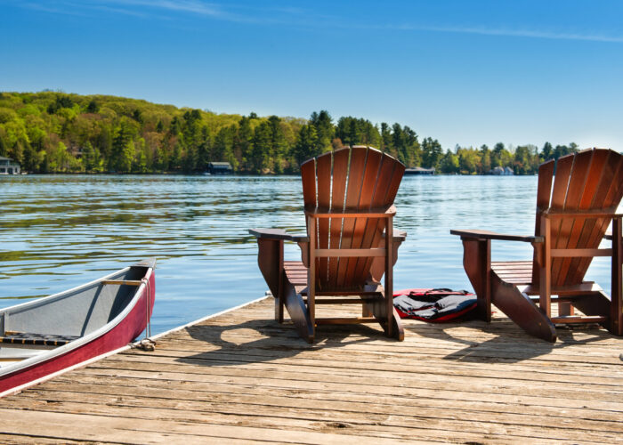Two Adirondack chairs sitting on a dock overlooking a lake