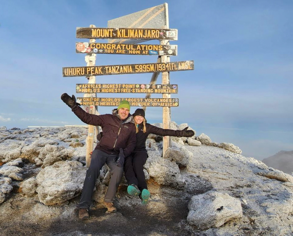 Two people posing happily at the summit of Mount Kilimanjaro on a clear day