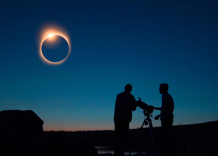 Silhouettes of people watching an eclipse through a telescope