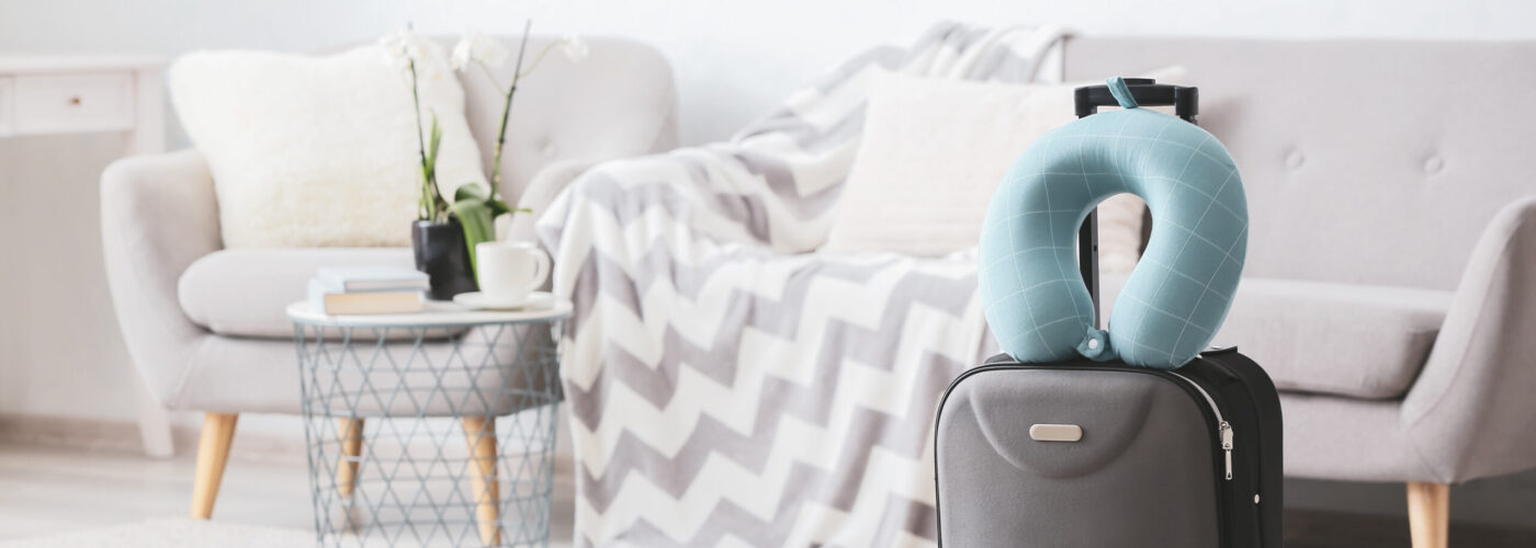 Travel neck pillow on top of rolling suitcase in light colored living room