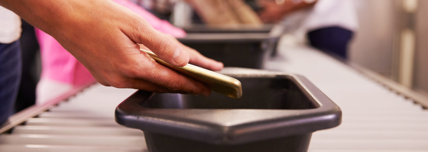 Close up of person's hands putting phone in airport security line bin