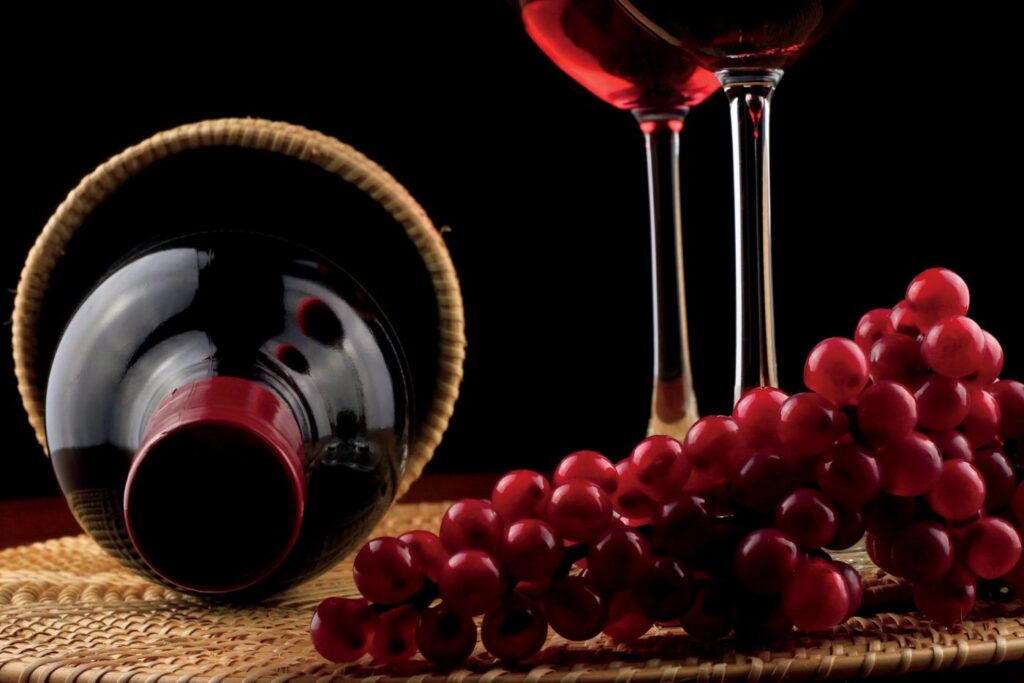 Bottle of wine resting on its side next to a full wine glass and a bunch of grapes