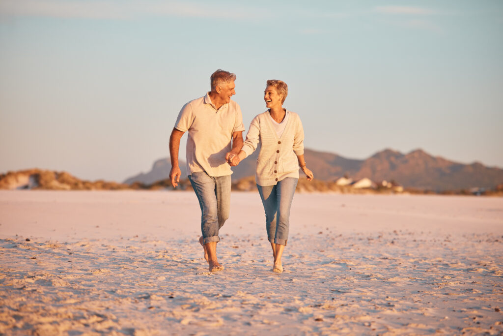 Elderly couple holding hands and walking on the beach at dusk