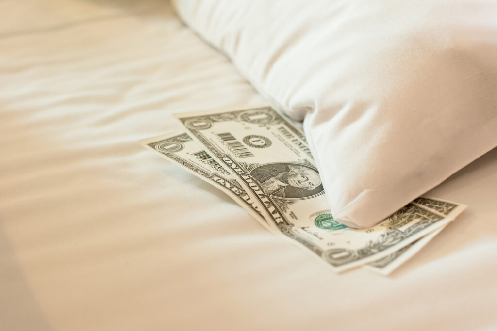 Two US dollars set beneath a white pillow on white bedsheets