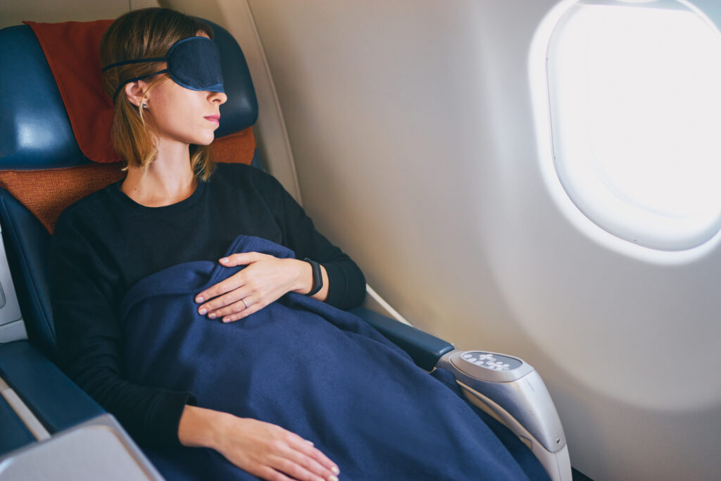 Woman sleeping on plane with a blanket and eye mask