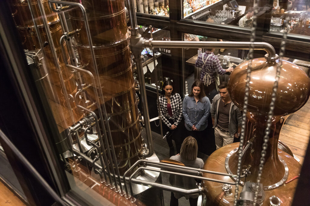 People listening to a tour guide describe the distilling process at Park Distillery Restaurant & Bar surrounded by metal distilling equipment