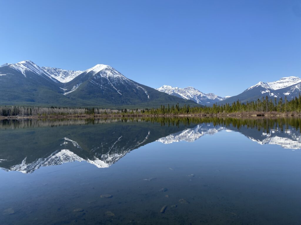 Mountains reflected in a lake on a clear blue day at Bow Valley Parkway