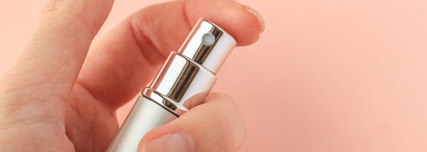 Close up of hand pressing the nozzle of a perfume atomizer on a pink backdrop