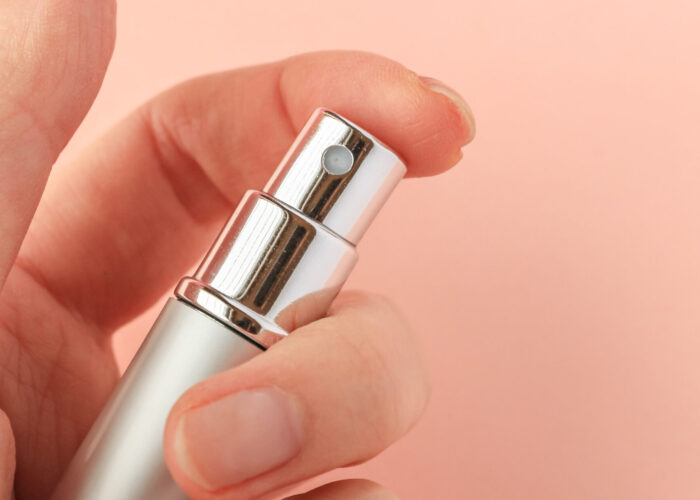 Close up of hand pressing the nozzle of a perfume atomizer on a pink backdrop