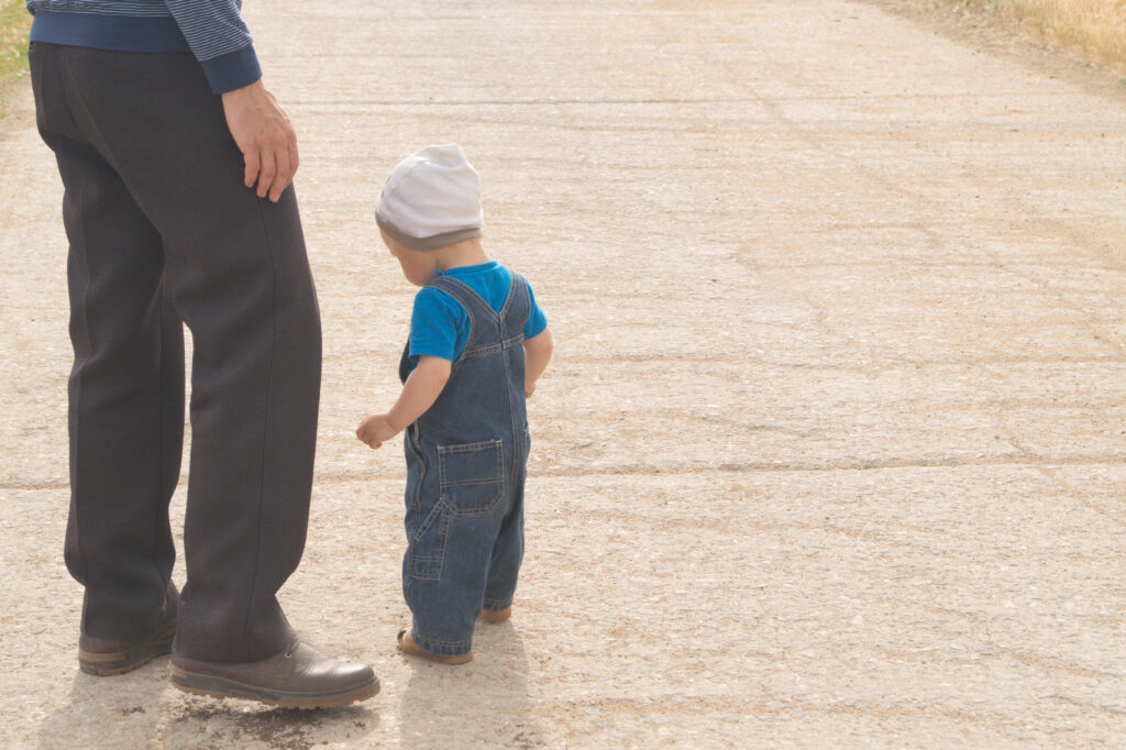 Close up of toddler walking next to father on wide sidewalk